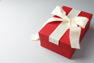 Beautiful gift box with beige bow on light grey background. Space for text