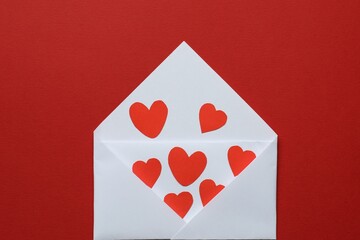 Valentine's Day. Envelope with many paper hearts on red background, top view