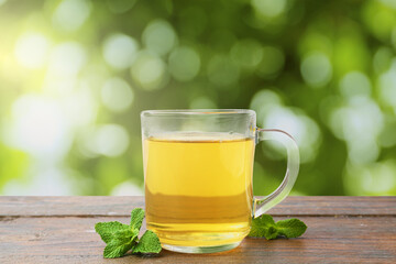 Aromatic mint tea in glass cup and fresh leaves on wooden table outdoors
