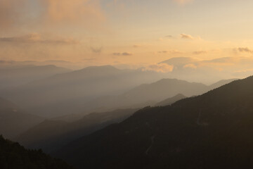 Misty mountain range with haze and clouds at sunset.