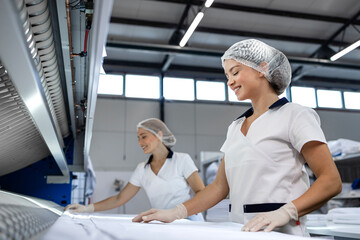 Obraz premium Female laundry workers folding linen and bedsheets after ironing in dry cleaning service.