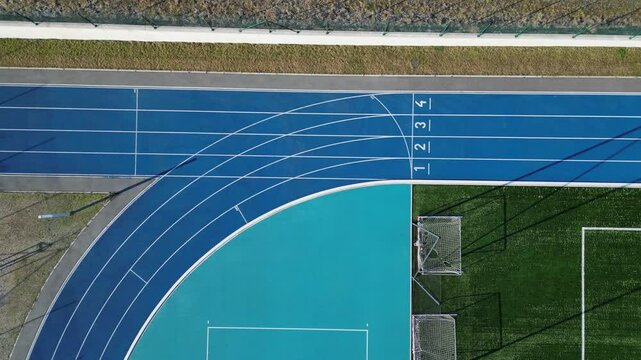 sports stadium with a running track with several lanes. inside oval there is a small football field for netball and handball with shield barriers. synthetic turf. view from top, all weather, rubber, 