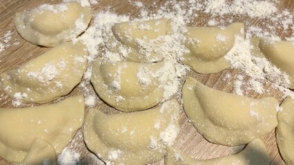 Close-up of freshly made homemade dumplings covered in flour, arranged on a wooden surface, ready for cooking, with soft warm lighting emphasizing texture and detail.