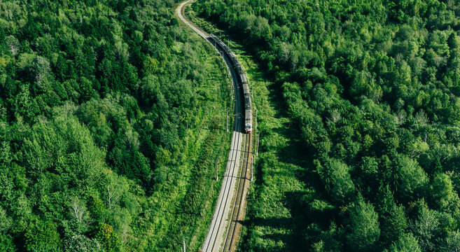 Aerial drone view of train in beautiful green summer forest. Long commuter train moving to railway station