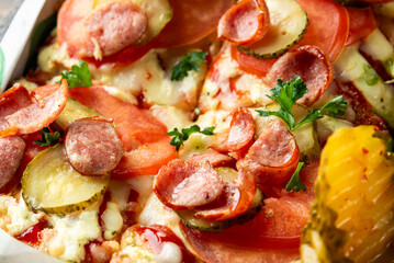 Delicious close-up of a freshly baked pizza topped with slices of pepperoni, fresh tomatoes, pickles, and sprinkled with herbs. Perfect for food lovers and culinary presentations.