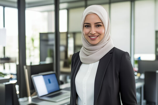 smiling Arab businesswoman wearing a hijab and stylish black blazer and white blouse, standing proudly in a modern office