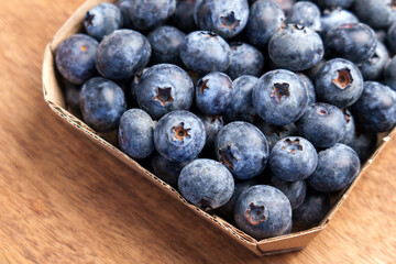 Fresh organic blueberries in a biodegradable cardboard container on a wooden surface. Healthy superfood rich in antioxidants. Close-up