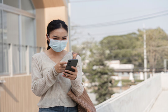 Young woman wearing a mask and texting on her smartphone outdoors in a public area.