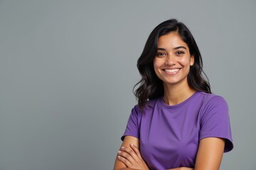 Portrait of a Cheerful Young Adult Woman with Long Black Hair Wearing a Purple T-Shirt Against a Gray Background, Exuding Confidence and Positivity