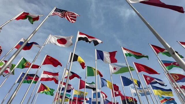 A collection of international flags waving on tall poles against a bright blue sky, symbolizing global unity and diversity.