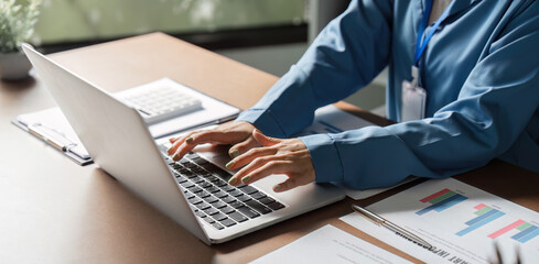 Business professional typing on laptop while managing reports and finances.