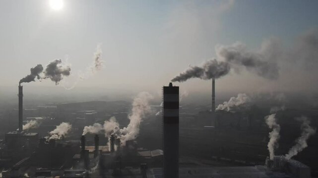 Industrial chimneys releasing smoke into atmosphere at sunrise