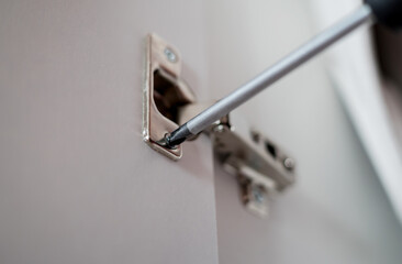 A detailed view of screwdriver to tighten a hinge on cabinet door