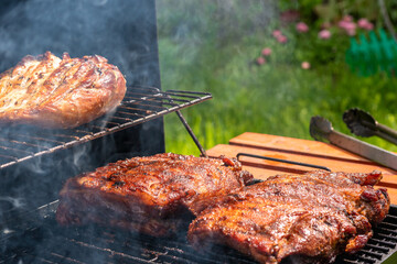 A grill is cooking meat, with a rack of ribs and a rack of chicken