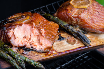 A piece of salmon is cut open on a wooden cutting board with a few pieces of asp