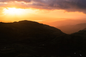 Golden morning light breaking through dramatic clouds over mountains of The Lake District, UK.