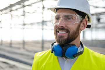 Smiling caucasian bearded engineer in protective glasses at the construction site