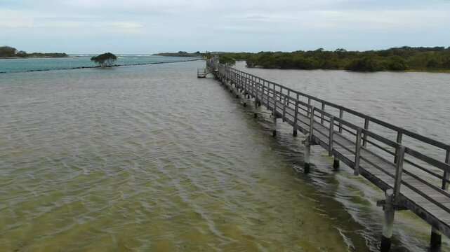 Urunga Boardwalk, wooden footbridge over Bellinger River, lagoon, Urunga, New South Wales, Australia. Aerial drone flying at low altitude along walkway
