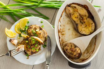 Homemade fish dish with lemon and herbs in a plate on a wooden table