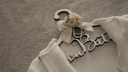 decorative baby hanger with a name cutout and bow holding a white knitted baby outfit