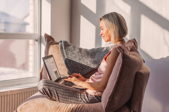 Happy dreamy middle aged woman sitting on sofa in living room with cup of tea or coffee - Powered by Adobe