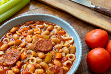Pasta with tomatoes, beans, and sausage in a blue bowl.