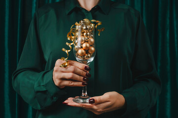 Woman holding glass filled with Christmas balls in front of green curtain