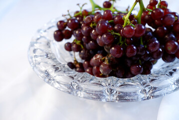 Grapes in glass bowl placed on white tablecloth. Close-up grape fruit texture and tableware glass. Champagne grapes for greeting, luxury, elegant, beautiful, kitchen, table setting, and white fabric.