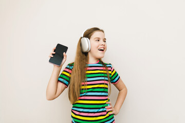 Naklejka premium Photo of a teenage girl holding a phone using modern technology, listening to the radio with headphones, wearing a striped tank top, on an isolated gray background