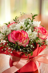 Closeup a Beautiful bouquet of flowers in a red box on a wooden table against light window at restaurant. Gift for holiday, birthday, Wedding, Mother's Day, Valentine's day, Women's Day. 