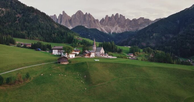 Landscape of Val di Funes in South Tyrol, Italy. Village and historic church among lush green valleys with impressive Dolomite Mountains. Time lapse drone flies towards the church.