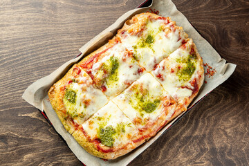 Delicious homemade pizza with melted cheese and vibrant green pesto, served in a parchment-lined tray. Perfect for sharing or enjoying alone, ideal for food photography.