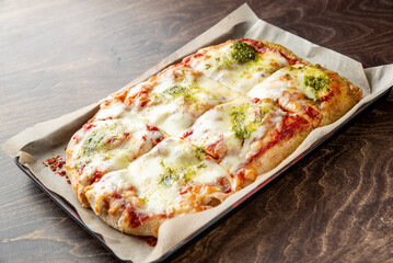 Delicious homemade pizza with melted cheese and vibrant green pesto, served in a parchment-lined tray. Perfect for sharing or enjoying alone, ideal for food photography.