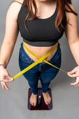 Woman measuring waist while standing on weight scale