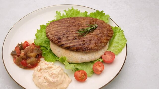 Serbian pljeskavica served with traditional Balkan side dishes. Balkan style burger pljeskavica grilled meat patty on a plate with Serbian salad and sauce