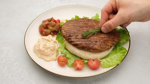 Serbian pljeskavica served on pita with traditional Balkan side dishes. Delicious Balkan style burger pljeskavica grilled meat patty decorated with rosemary