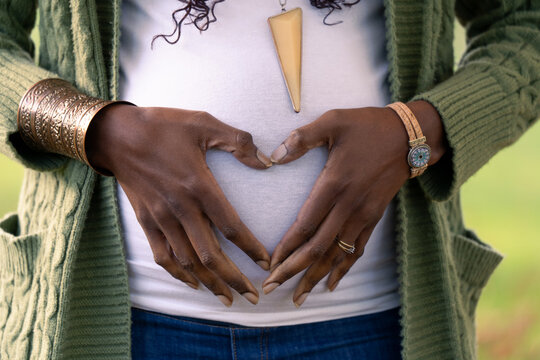 A pregnant woman holding her belly, forming a heart shape with fingers