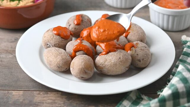 Papas arrugadas con mojo. Canary Islands potatoes. Pouring mojo picon sauce on potatoes