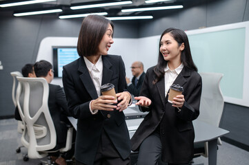 Two businesswomen standing in a group meeting around a table in a modern office. There are documents, laptops. Everyone is brainstorming, planning sales, digital marketing and growth strategies.