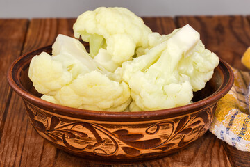 Blanched cauliflower pieces in bowl on rustic table, front view