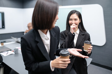 Two businesswomen standing in a group meeting around a table in a modern office. There are documents, laptops. Everyone is brainstorming, planning sales, digital marketing and growth strategies.