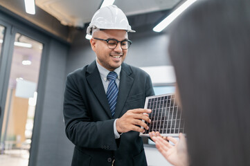 Male and female engineers discussing solar panel system in office with documents, laptops, sales...