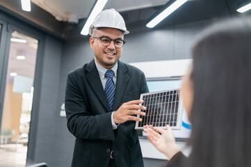 Male and female engineers discussing solar panel system in office with documents, laptops, sales...
