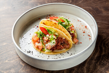 Delicious beef tacos served on a white plate, topped with fresh lettuce, tomatoes, and a dollop of sauce. Perfect for a flavorful meal or a festive gathering.