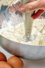 The cook mixes cottage cheese with a mixer to obtain a homogeneous mass