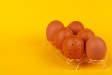 Six brown eggs in a holder on a yellow background, highlighting the impact of increasing egg prices on American households