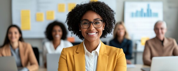 A confident woman in a yellow blazer smiles in a modern office, surrounded by colleagues engaged in a collaborative work environment.