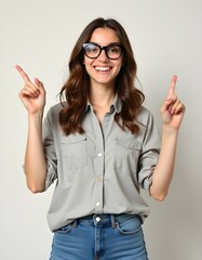 Enthusiastic Woman with Glasses Pointing Upward: Smiling Brunette in Gray Shirt and Jeans Directing Attention Above 