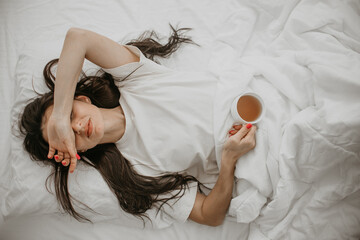 Woman lying in bed with coffee cup, relaxing morning vibes