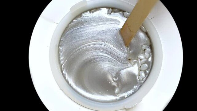 A wooden spatula stirs the wax granules and melted wax for depilation in the wax melter